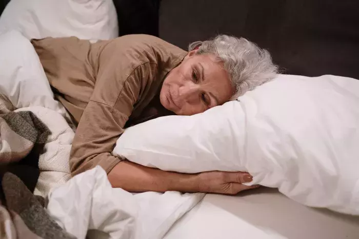 Femme agée éveillée dans son lit en pleine nuit, les yeux ouverts dans l'obscurité.