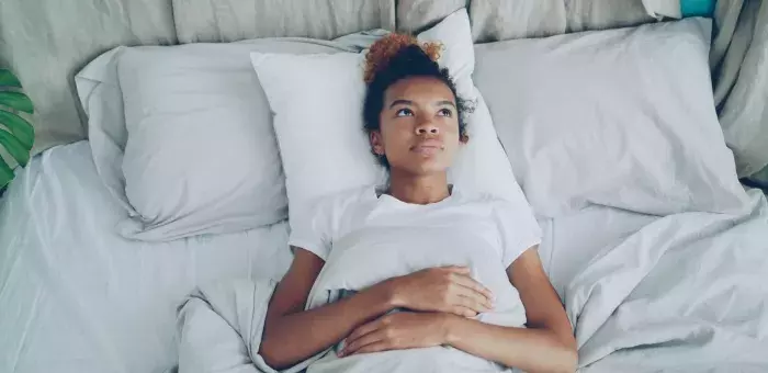 Femme allongée dans son lit, les yeux ouverts fixant le plafond, éveillée malgré la fatigue.